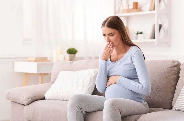 Gravid dam känner sig sjuk sitter på soffan inomhus — Stockfoto