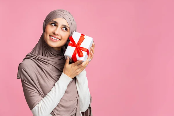 Neugierige muslimische Mädchen im Hijab schüttelt Geschenkbox und fragt sich, was drinnen ist — Stockfoto