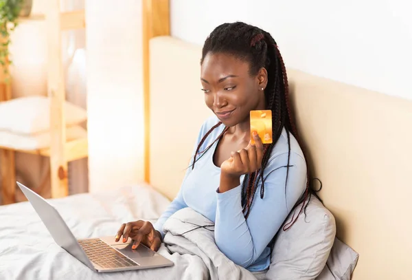 Signora utilizzando computer portatile e carta di credito seduto a letto al coperto — Foto Stock