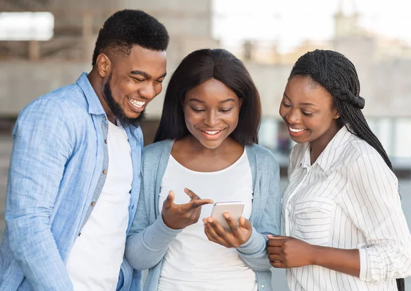Millennial afro ragazza mostrando contenuti divertenti su smartphone agli amici — Foto Stock
