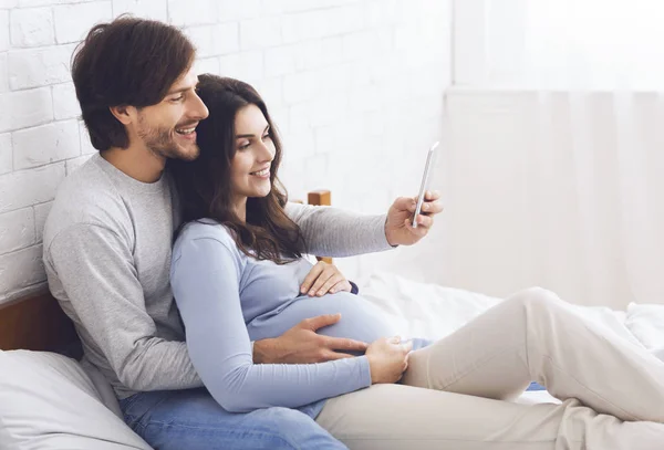 Hamile çift evde akıllı telefonuyla dinleniyor. — Stok fotoğraf