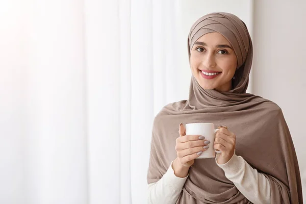 Wanita arab yang santai dalam hijab dengan secangkir kopi di dekat jendela — Stok Foto