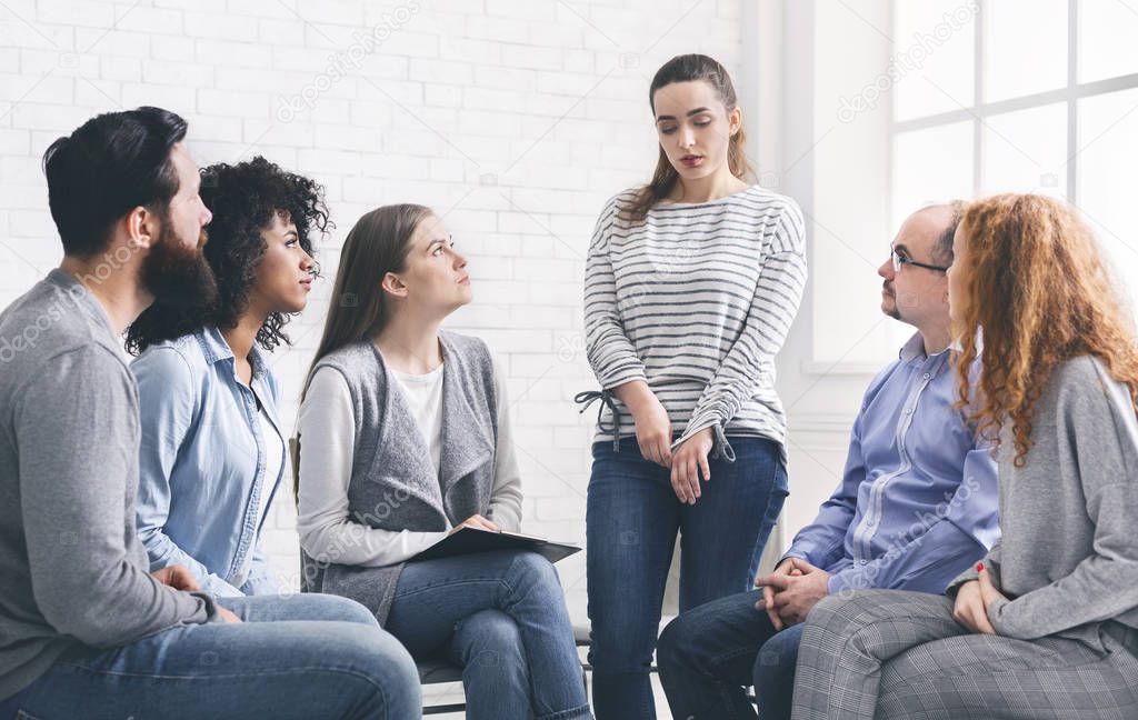 Addict woman talking to group at therapy session