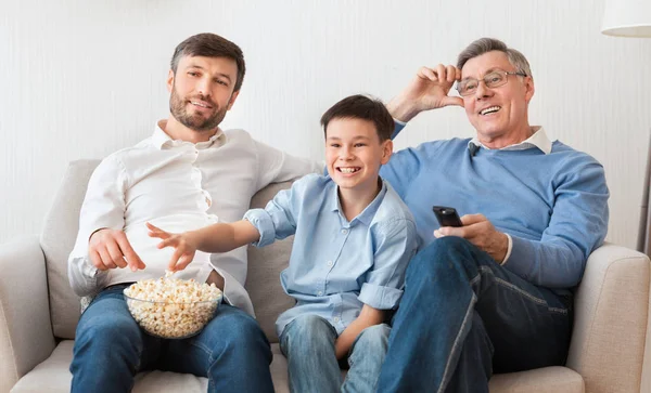Grand-père, père et fils regardant la télévision assis sur le canapé intérieur — Photo