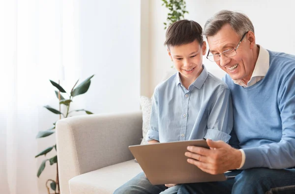 Дедушка и внук просматривают интернет, сидя дома на диване — стоковое фото