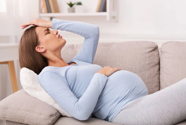 Mujer embarazada tocando la frente teniendo migraña acostada en un sofá — Foto de Stock