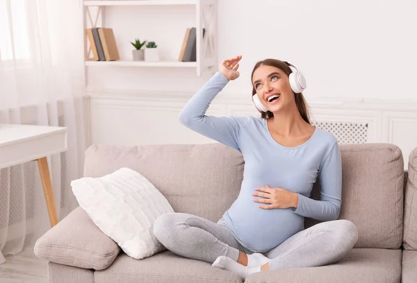 Mãe alegre-To-Be em fones de ouvido ouvir música sentada no sofá — Fotografia de Stock