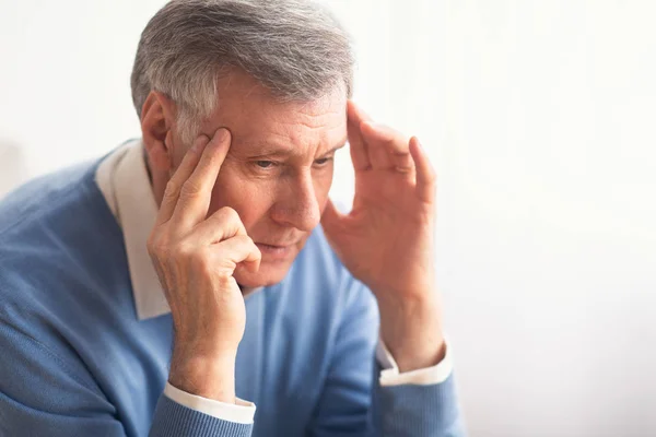 Senior Gentleman, der an Migräne leidet, sitzt vor weißem Hintergrund — Stockfoto