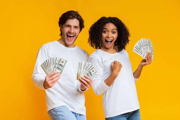 Emocionada pareja interracial sosteniendo mucho dinero en efectivo, celebrando el éxito juntos — Foto de Stock