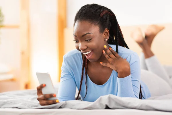 Emocionado chica negra leyendo mensaje en el Smartphone acostado en la cama —  Fotos de Stock