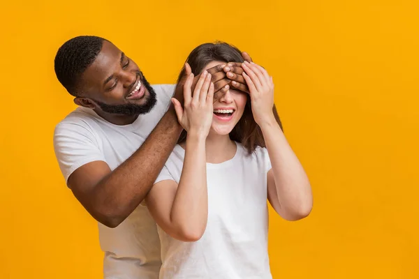 Cuidando afro marido surpreendendo sua esposa, cobrindo seus olhos com as mãos — Fotografia de Stock