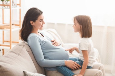 Anaokulu kızı hamile annenin karnını işaret ediyor.