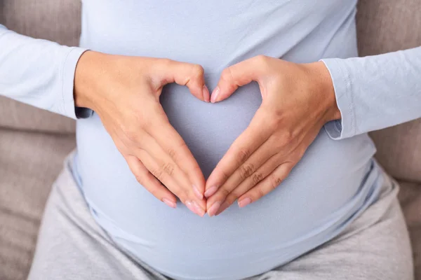 Nierozpoznawalna kobieta w ciąży trzymając się za ręce na brzuchu tworząc serce, widok z góry — Zdjęcie stockowe