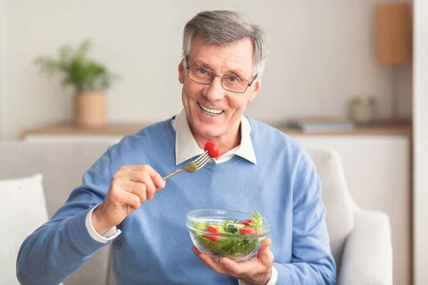 Senior Man Eating Vegetable Salad Sitting On Couch At Home