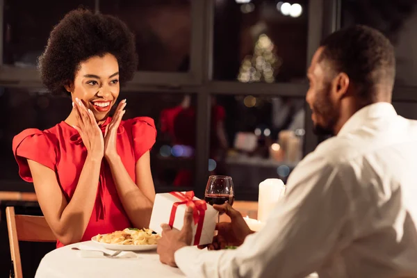 Мужчина, дарящий подарок девушке, имеющей романтическое свидание в ресторане — стоковое фото