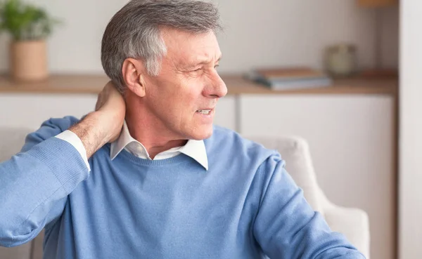 Senior man masseren nek lijden van pijn zitten op de bank — Stockfoto