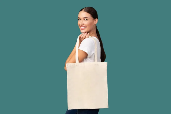 Chica sosteniendo blanco Eco bolso de mano de pie sobre fondo turquesa —  Fotos de Stock