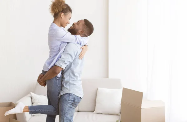 Afro esposo levantando esposa de pie entre cajas móviles en apartamento —  Fotos de Stock