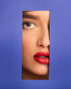 Dolgun kırmızı dudaklı kadın mavi kağıtta deliğe bakıyor.