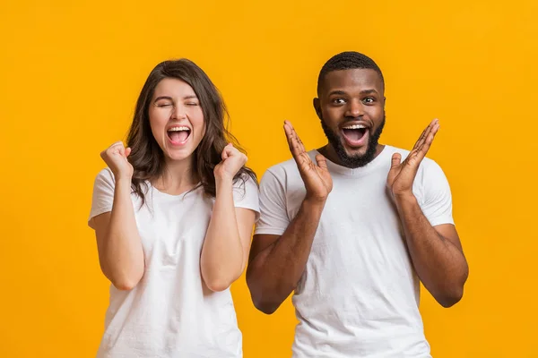 Gemischtes Paar jubelt über Erfolg, feiert emotional gute Nachrichten vor gelbem Hintergrund — Stockfoto