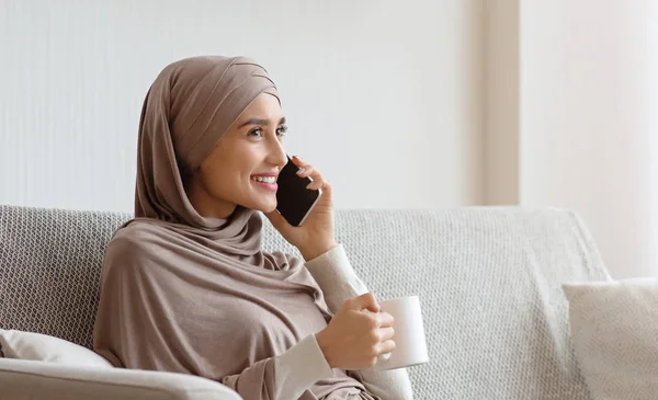 Gadis berjilbab berbicara di ponsel dan minum teh di rumah — Stok Foto
