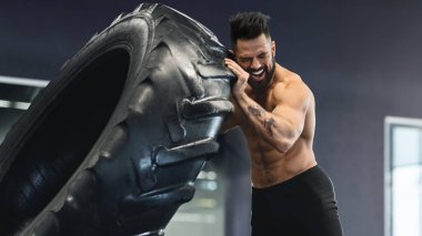 Genç kaslı adamın spor salonunda tekerlek kamyonu egzersizleri.