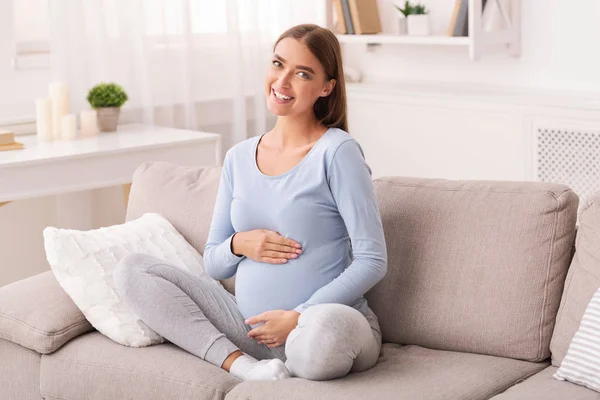 Menina grávida tocando barriga sorrindo sentado no sofá em casa — Fotografia de Stock