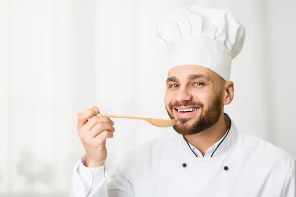 Chef Man degustação de alimentos segurando colher de pé contra janela interior — Fotografia de Stock