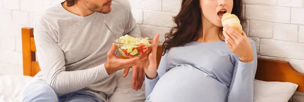 Mujer embarazada rechazando ensalada de verduras frescas y comiendo croissant —  Fotos de Stock