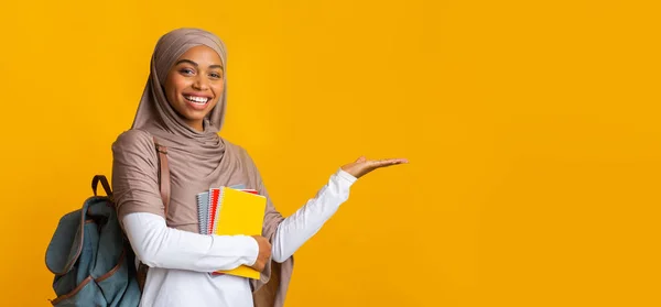 Alegre preto islâmico feminino estudante no hijab apontando de lado com a mão — Fotografia de Stock