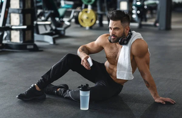 Handsome hot guy resting at gym with phone and water