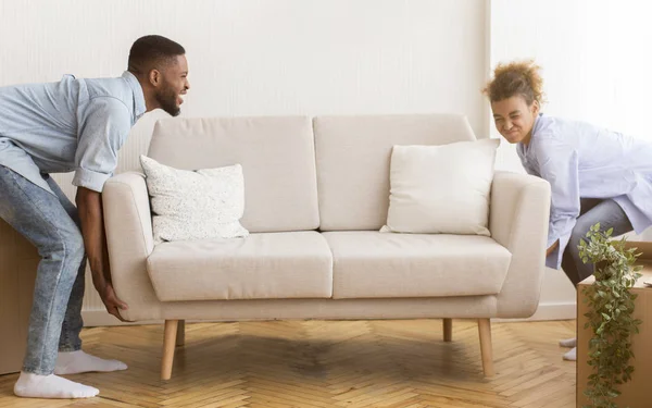 Афроамериканские супруги поднимают тяжелые диваны в новых апартаментах — стоковое фото