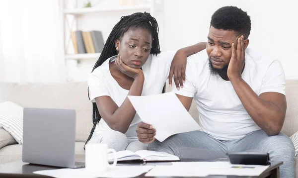 Niedergeschlagenes schwarzes Paar schaut zu Hause auf Rechnung und ärgert sich über Rechnungen — Stockfoto