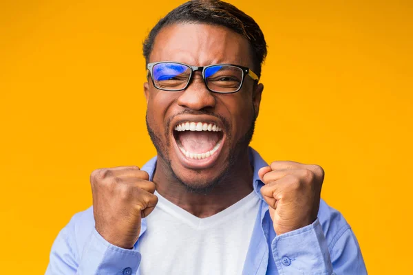 Emotionele zwarte man schreeuwen schudden vuisten staande op oranje achtergrond — Stockfoto