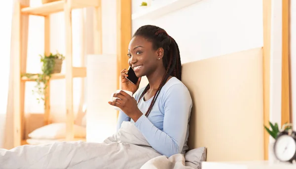 Afro-americano donna chat su cellulare avendo caffè a letto — Foto Stock
