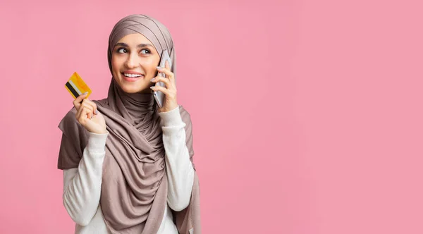 Elinde kredi kartı tutan ve cep telefonuyla konuşan tesettürlü Müslüman kadın. — Stok fotoğraf