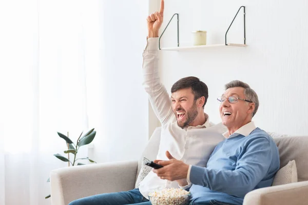 Filho adulto e pai sênior assistindo TV esportiva em casa — Fotografia de Stock