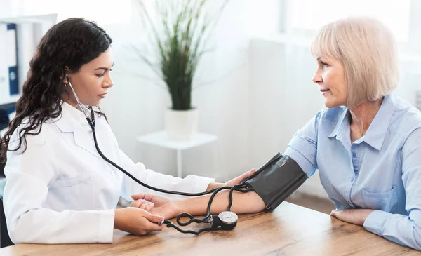 Žena zdravotní sestra kontrolu krevního tlaku dospělé ženy — Stock fotografie
