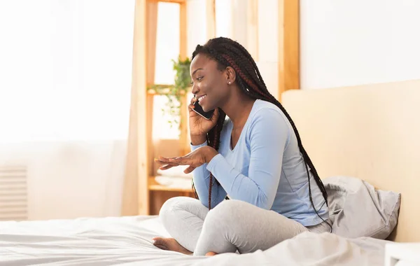 Afro Girl hablando por celular sentado en la cama en el dormitorio —  Fotos de Stock