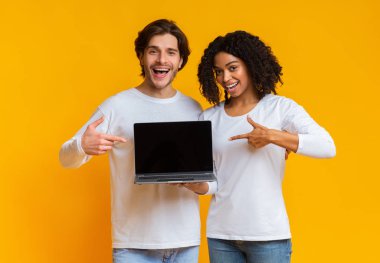 Gülümseyen çok ırklı çift siyah ekranlı dizüstü bilgisayarı işaret ediyor