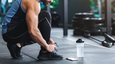 Spor salonunda ayakkabı bağcığı bağlayan bir sporcu.