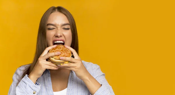 Jovem senhora mordendo hambúrguer desfrutando de junk food, panorama, Studio Shot — Fotografia de Stock