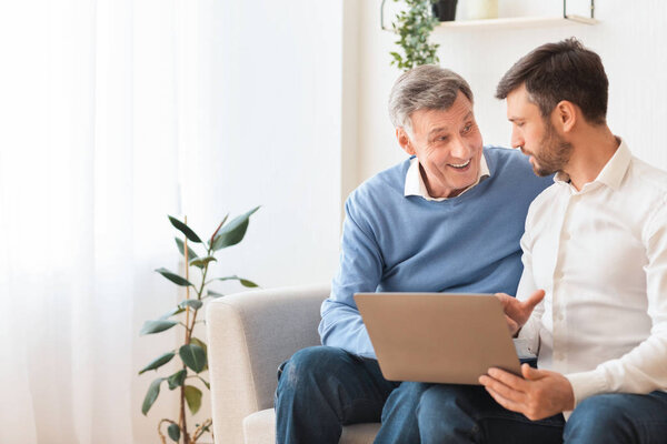 Old Man And Adult Son Using Laptop Sitting At Home