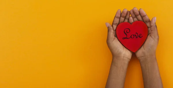 Mulher segurando coração de madeira vermelho com amor inscrição em palmas — Fotografia de Stock