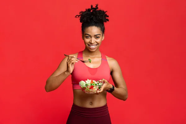Friska sportig flicka äter grönsaker sallad över röd bakgrund — Stockfoto