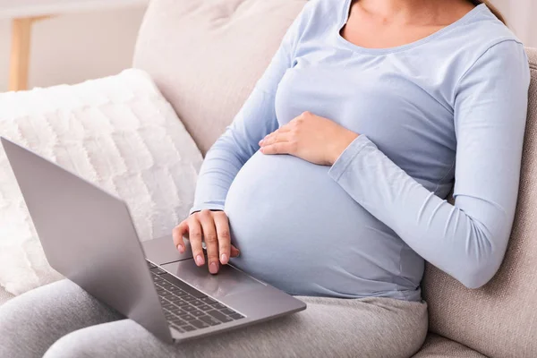 Нерозпізнана вагітна леді за допомогою ноутбука сидить на дивані в приміщенні — стокове фото