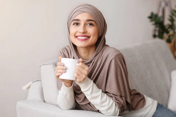 Boldog muszlim lány hidzsábban otthon teázik. — Stock Fotó