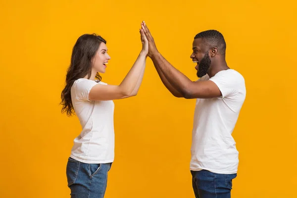 Glad interracial par ger high-five till varandra, firar gemensam framgång — Stockfoto