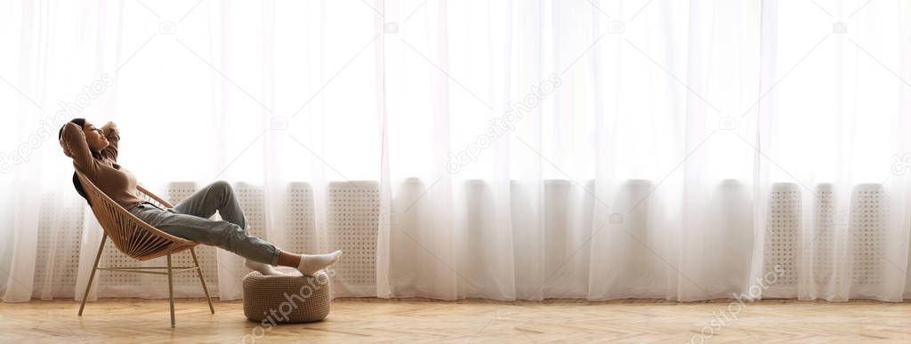 Young Asian Girl Relaxing In Modern Wicker Chair Near Window