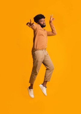Havalı siyah adam zıplarken barış jesti yapıyor.